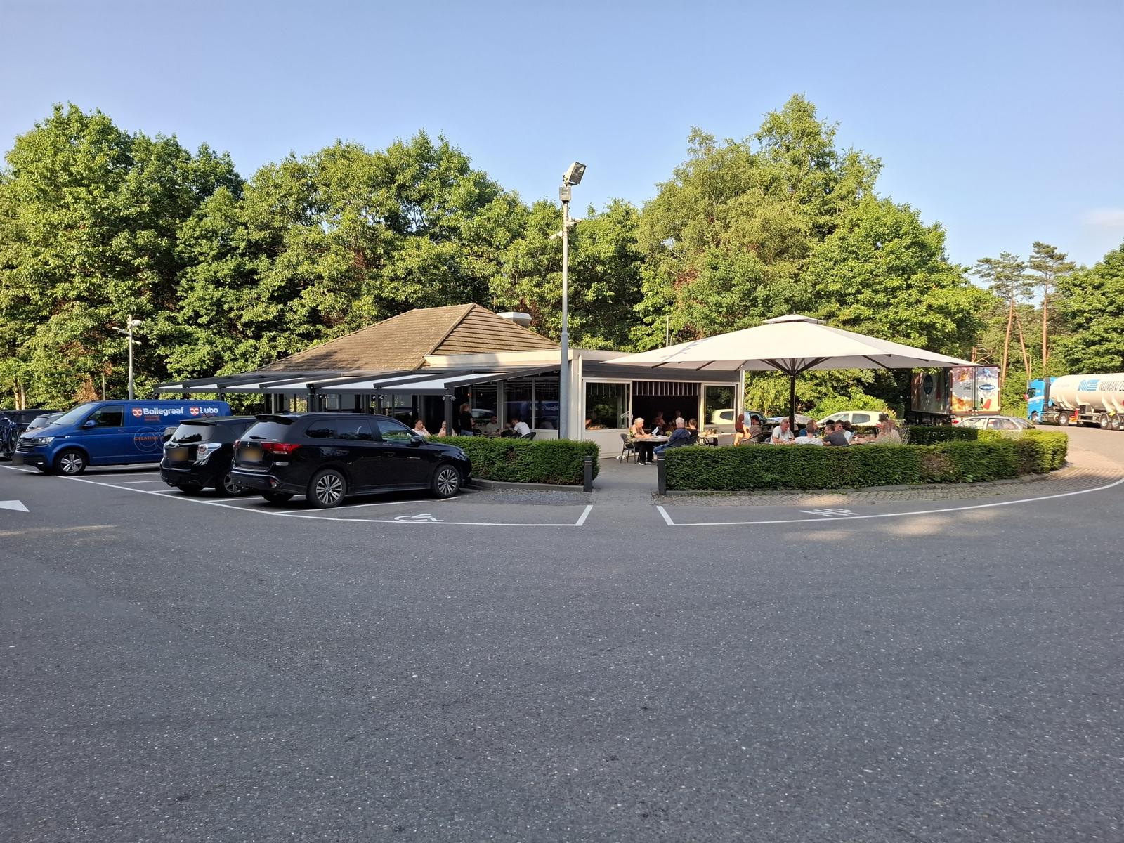 Wegrestaurant Mendel van buiten, met het terras onder de parasol en de parking ervoor
