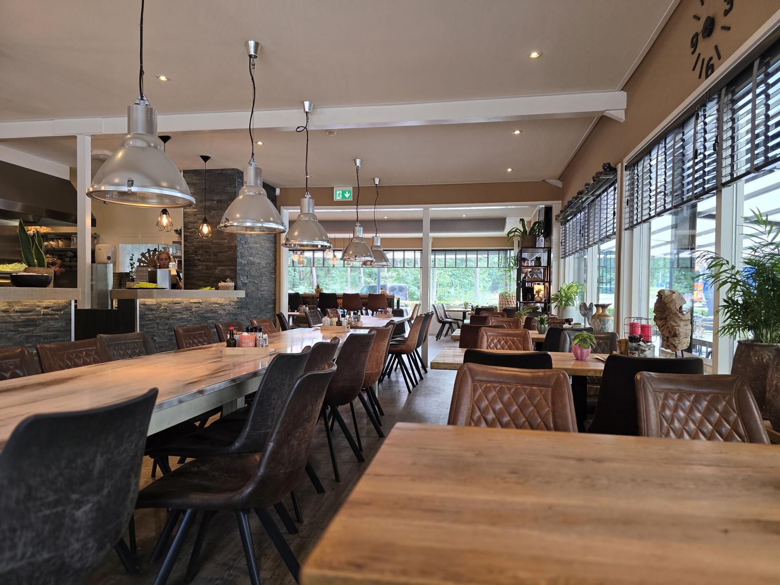 Het restaurant van binnen: lange houten tafels, leren stoelen, industriële lampen en grote ramen